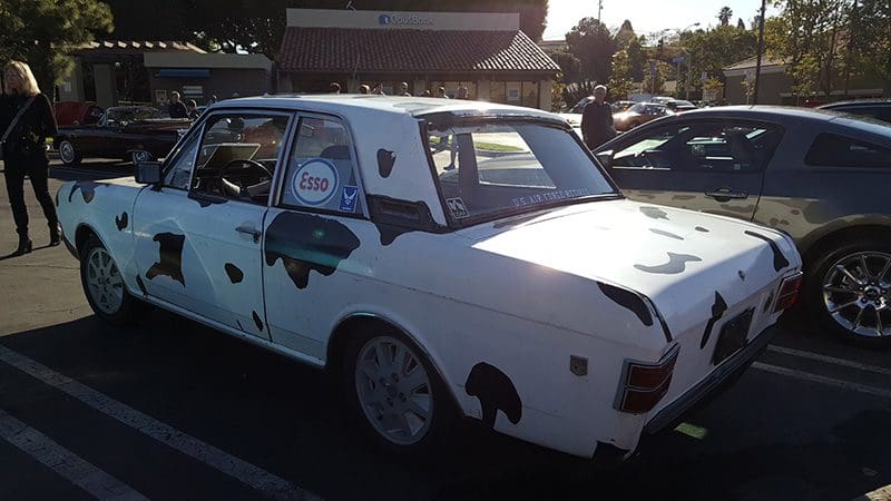 A classic white car with black spots mimicking a cow's pattern.