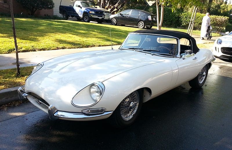 Classic white Jaguar E-Type parked on a sunny street.