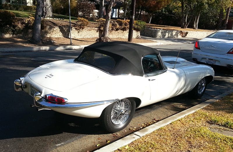 Classic white convertible car parked on a street with a soft top.