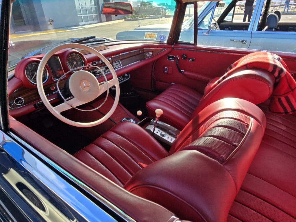 Classic car interior with red leather seats and white steering wheel.