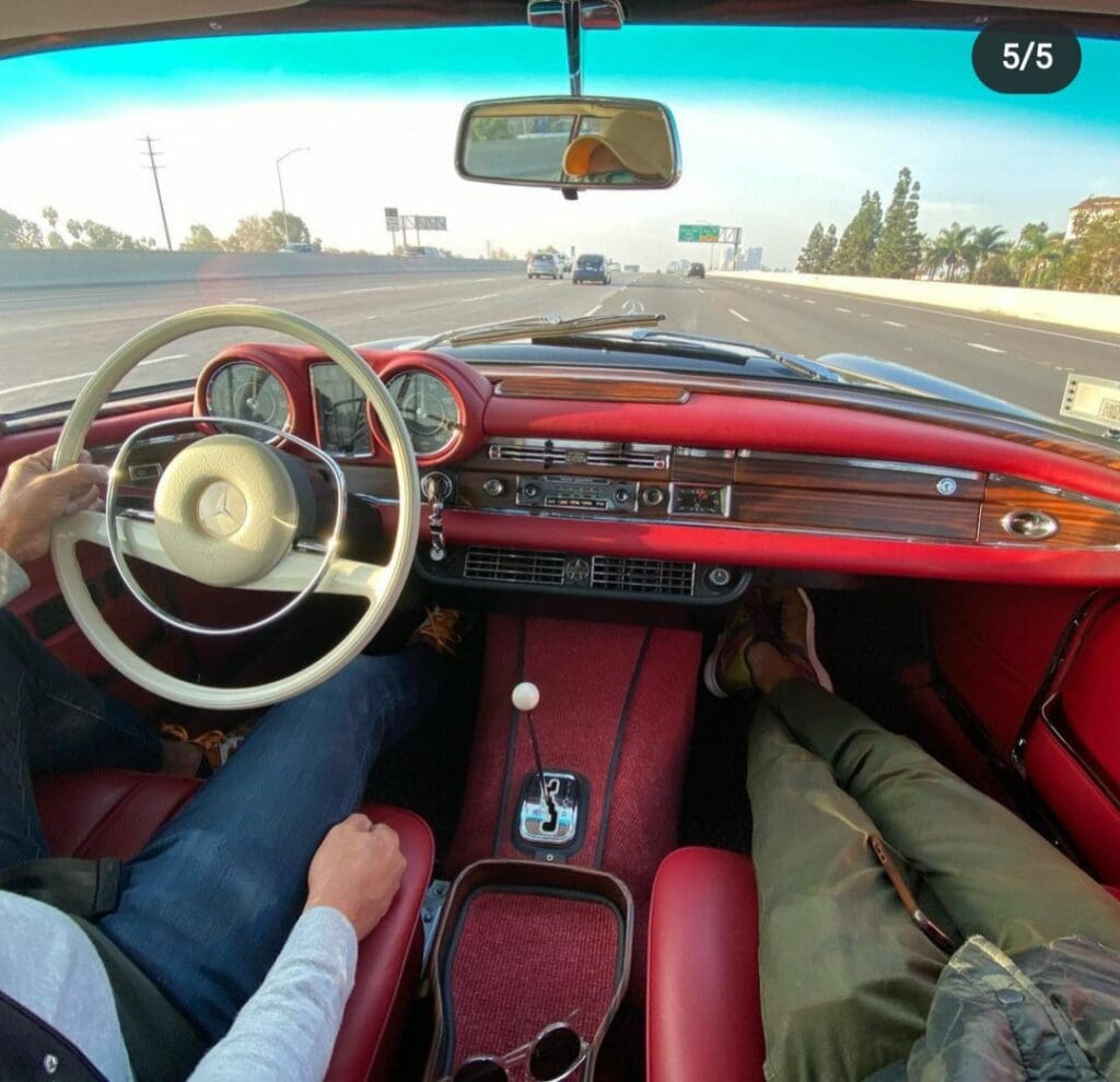 View from inside a vintage red car with two passengers on a sunny day.
