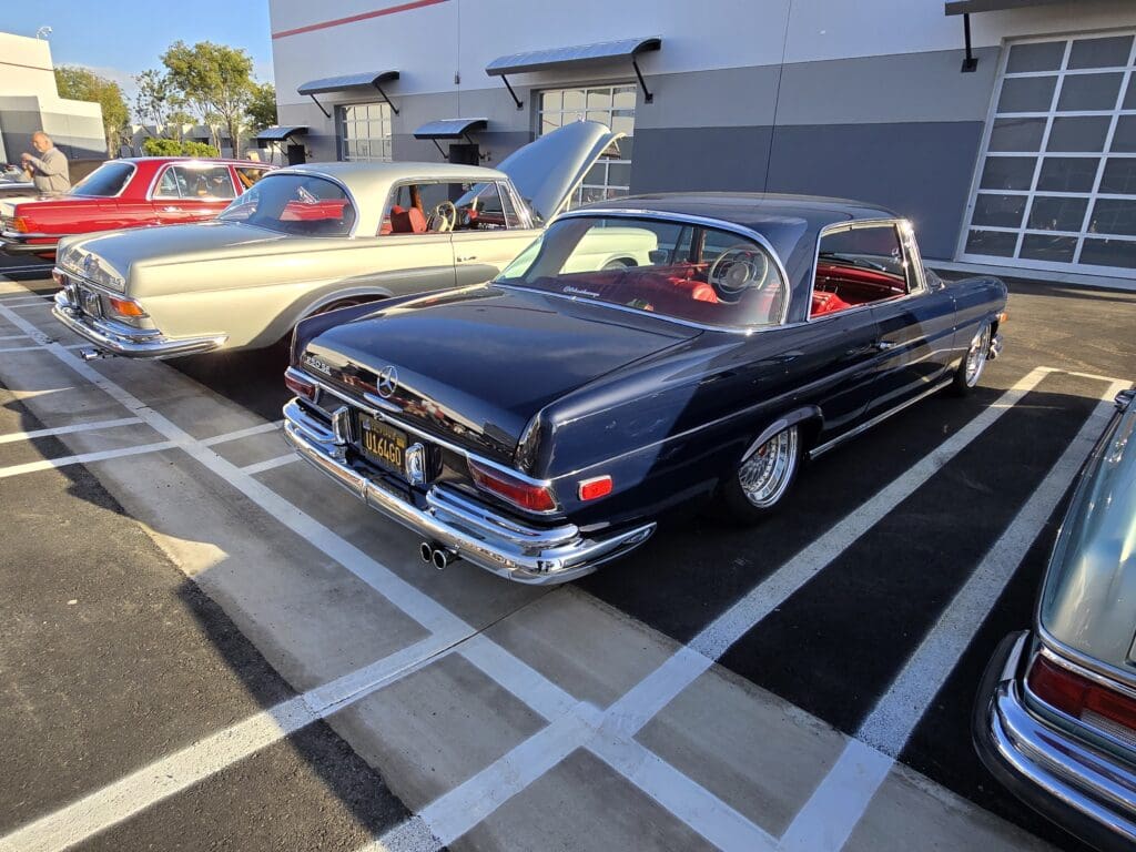 Classic black vintage car parked alongside another classic car in a parking lot.