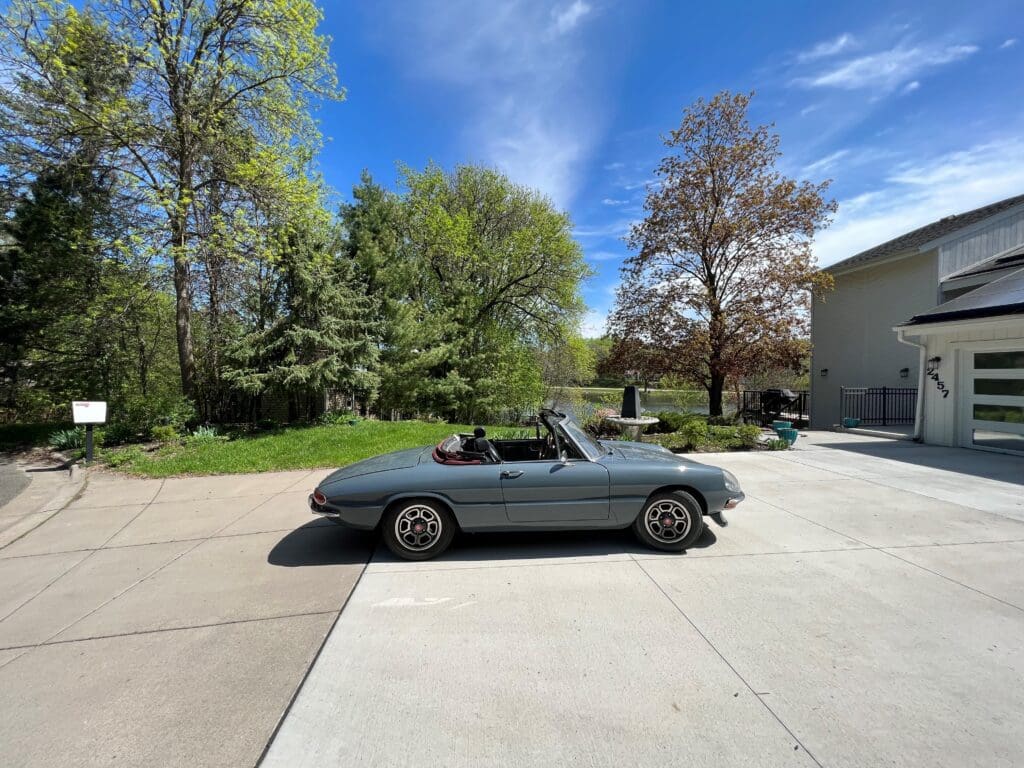 A vintage convertible car parked on a driveway under clear blue sky.