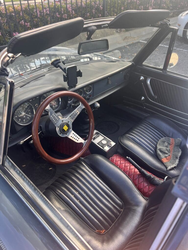 Classic car interior with wooden steering wheel and vintage dashboard.