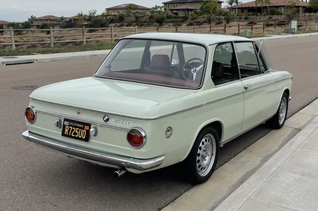 White vintage BMW 2002 parked by the roadside with a scenic background.