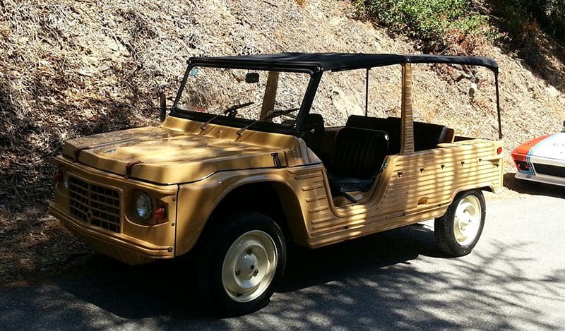 A vintage yellow off-road vehicle parked on a sunny road.