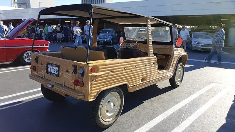 Vintage wooden-bodied car parked outdoors near a bridge.