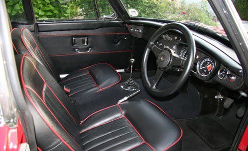 Interior of a classic car with black leather seats and red stitching.