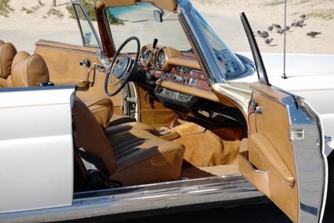 Interior of a classic car with brown leather seats and wooden dashboard.
