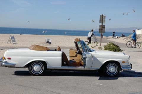 Classic white convertible car parked by the beach with the ocean in the background.