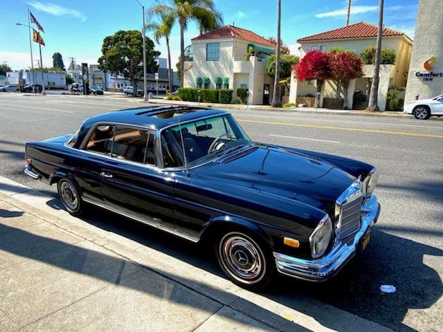 Vintage black luxury car parked on a sunny street.