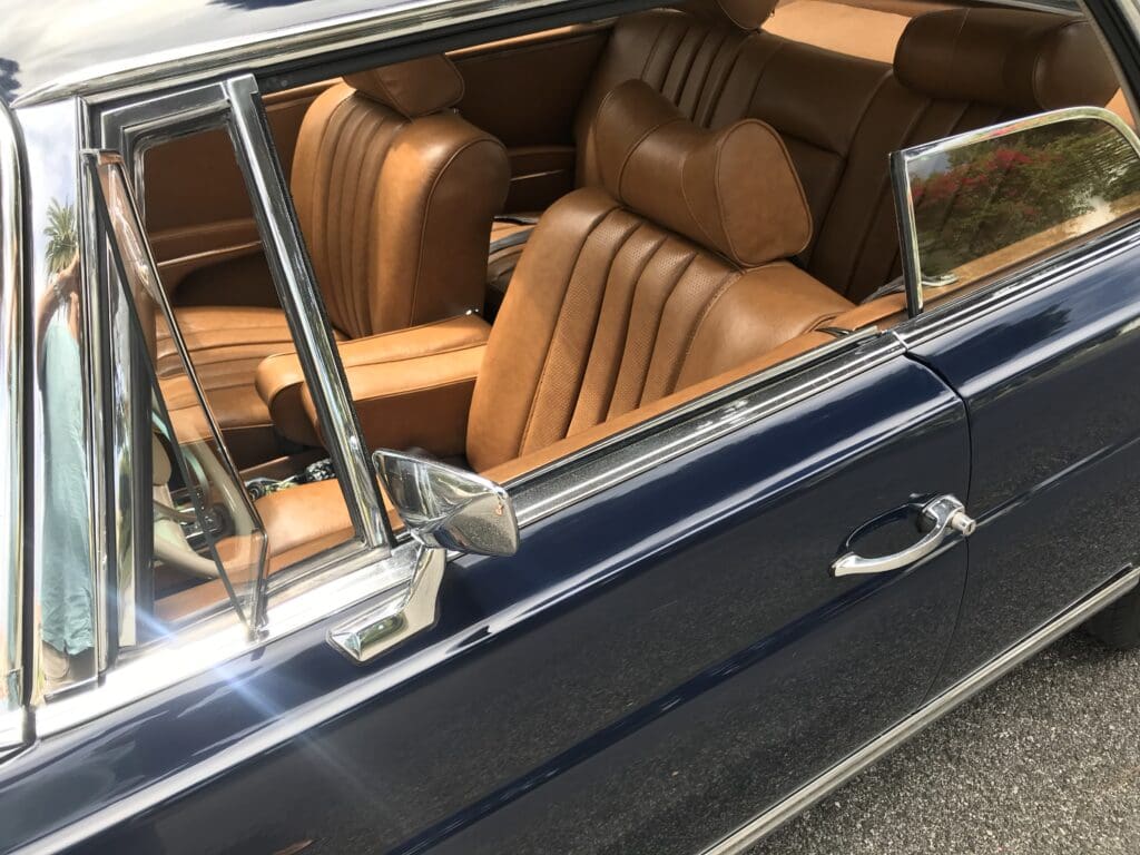 Close-up of a classic car's brown leather interior and open window.