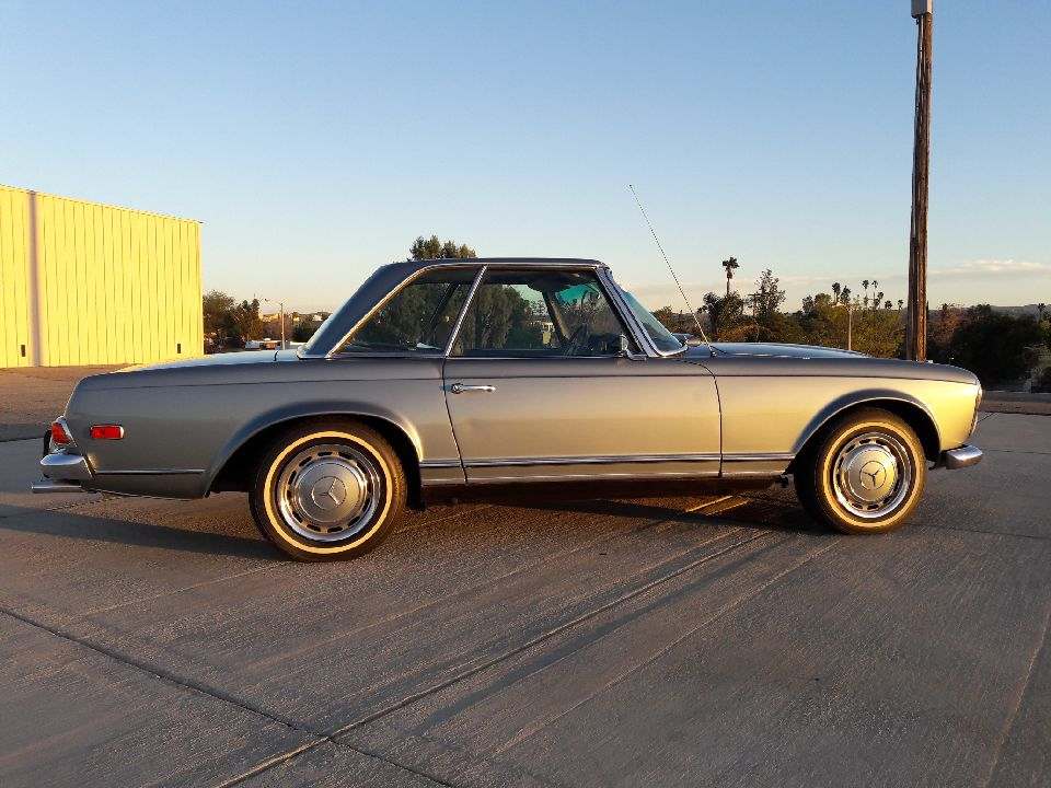 Classic silver convertible car parked on a concrete surface at sunset.