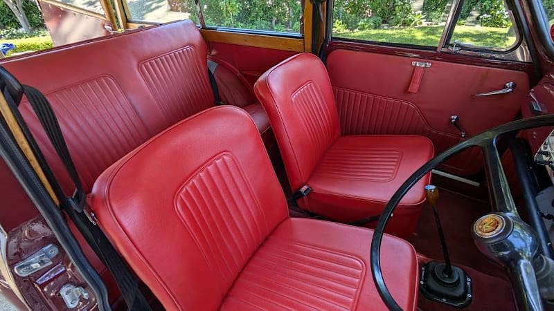 Red leather seats inside a vintage car with a steering wheel.