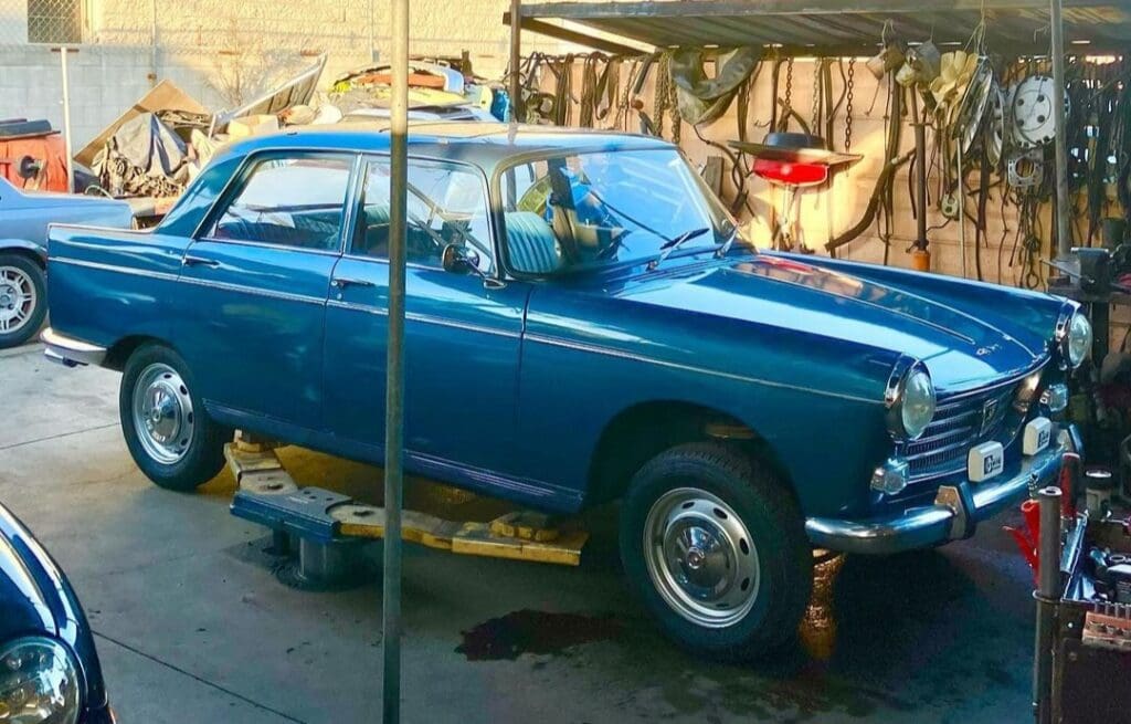 Vintage blue car parked under a canopy in a rustic setting.