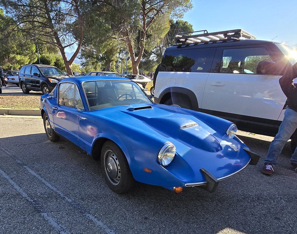 Blue vintage sports car parked beside a white SUV outdoors.