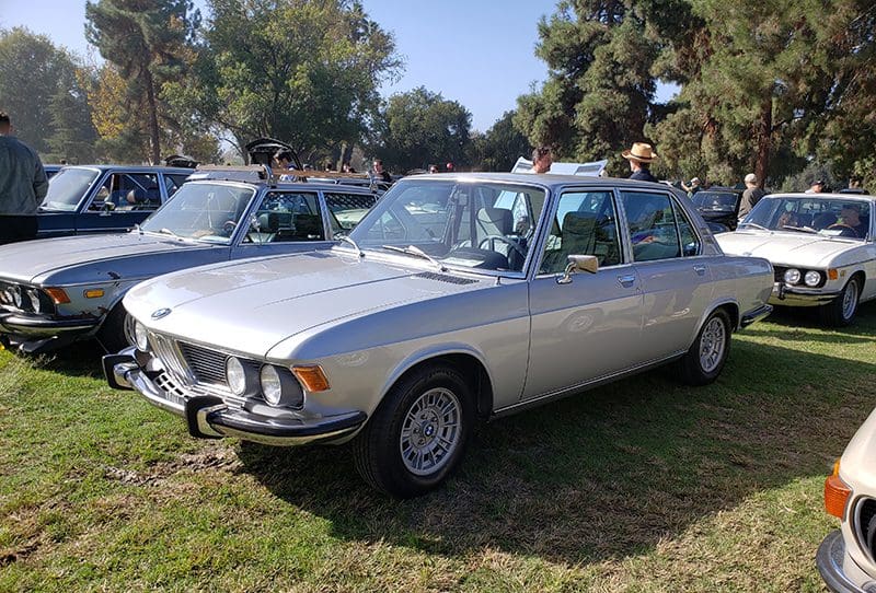 Silver classic BMW parked on grass at a car show.