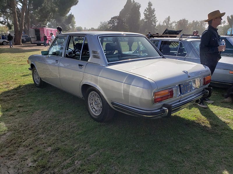 Silver classic BMW parked on grass at a car show.