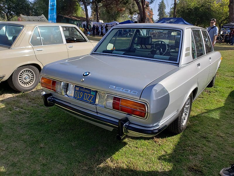 Classic silver Mercedes-Benz parked on grass at a sunny outdoor event.