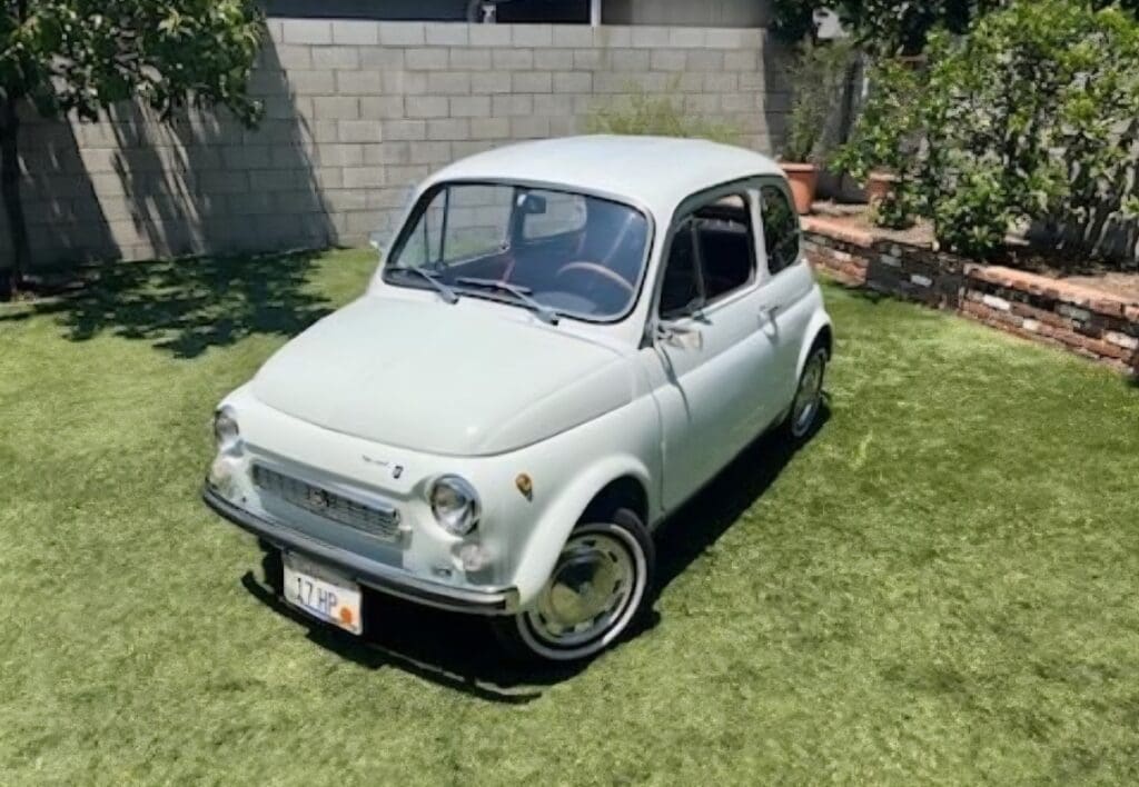 Classic white Fiat 500 parked on green grass in a sunny yard.