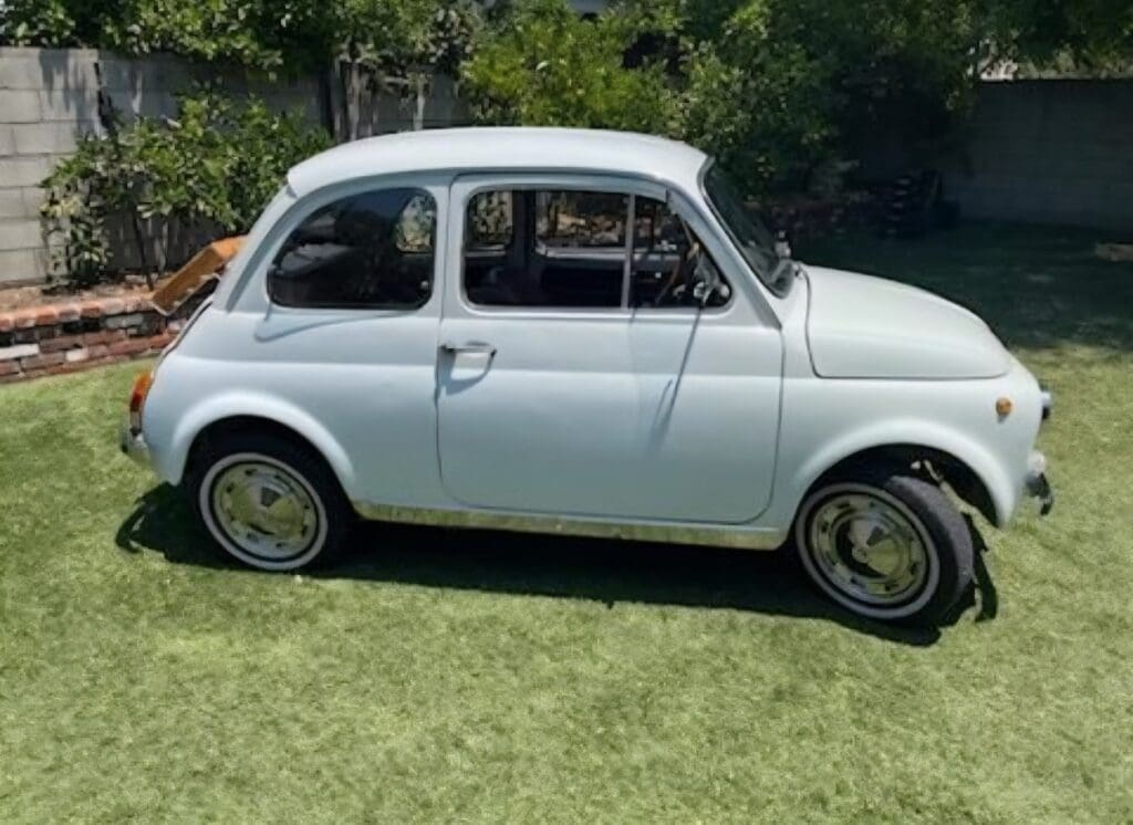Classic white vintage car parked on grass under sunlight.