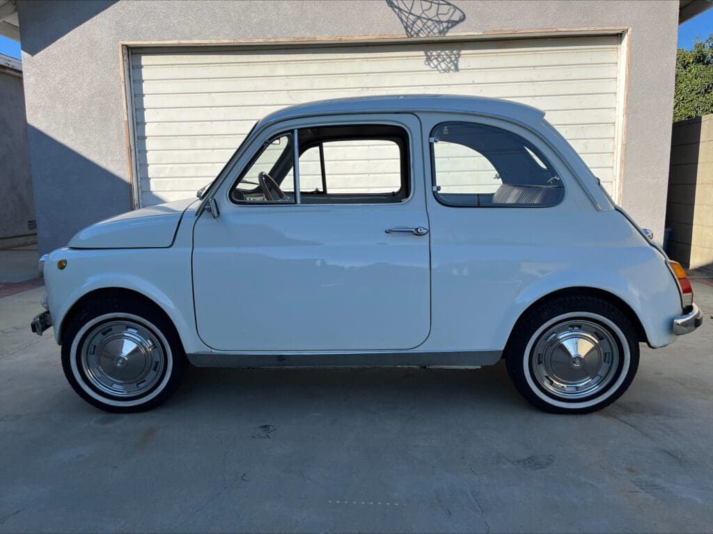 A classic light blue vintage car parked in front of a garage.