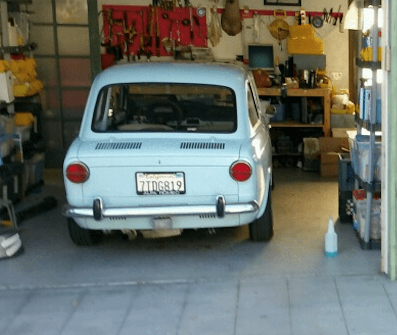 A blue vintage car parked inside a cluttered garage.