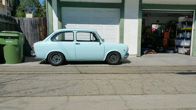 Light blue vintage car parked beside a building with garage doors.