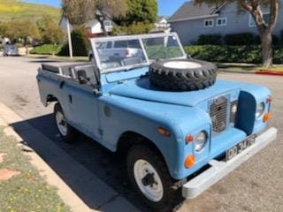 Light blue vintage Land Rover parked on a suburban street.