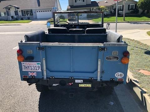 Rear view of a vintage blue Jeep with open back seats on a sunny day.