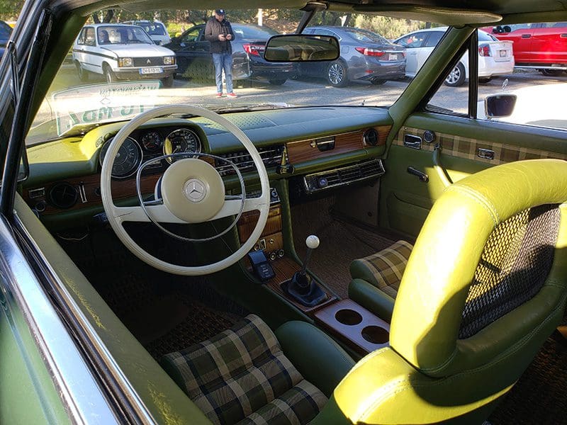Interior view of a vintage car with a yellow seat and classic steering wheel.