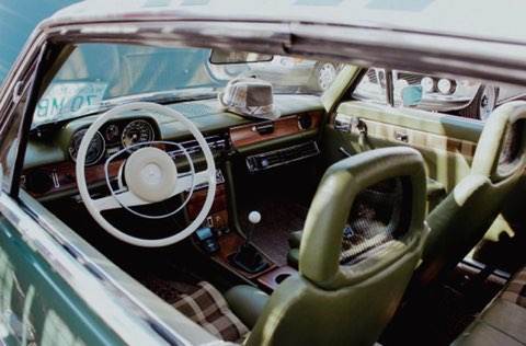 Vintage car interior with green leather seats and a classic steering wheel.