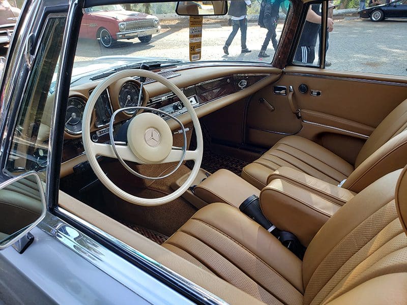 Interior of a classic car with tan leather seats and a white steering wheel.