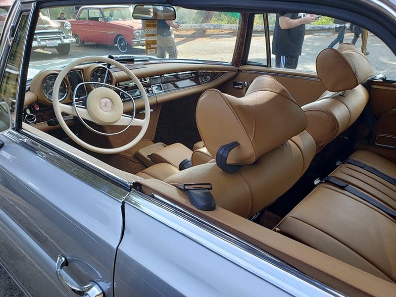 Classic car interior with tan leather seats and vintage steering wheel.