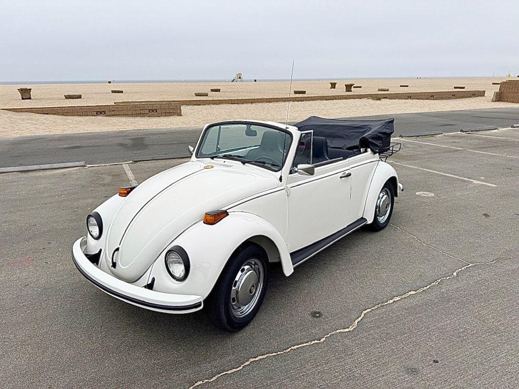 Classic white Volkswagen Beetle convertible parked by the beach.