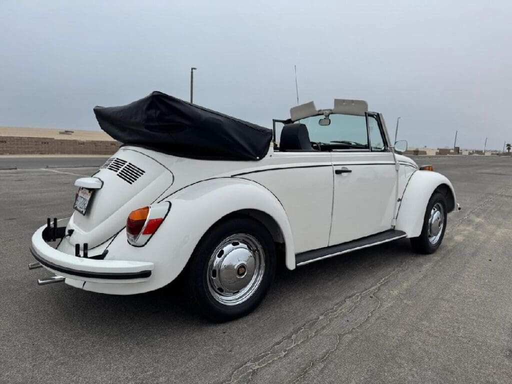 White classic Volkswagen Beetle convertible with black soft top on a road.