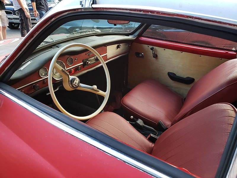 Classic car interior with vintage steering wheel and plush seats.
