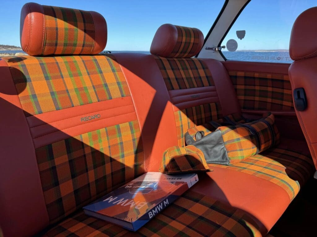 Vintage car interior with plaid upholstery and orange seat belts.