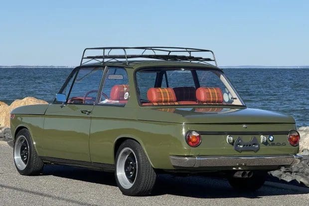 A classic olive green car with a roof rack parked by the sea.