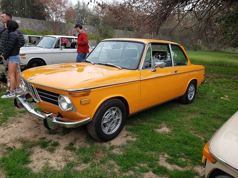 A classic yellow BMW 2002 car parked on grass with a person nearby.