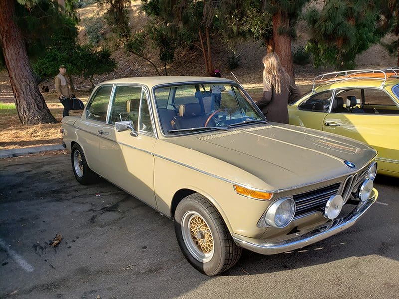 Classic beige vintage car parked outdoors with trees in background.