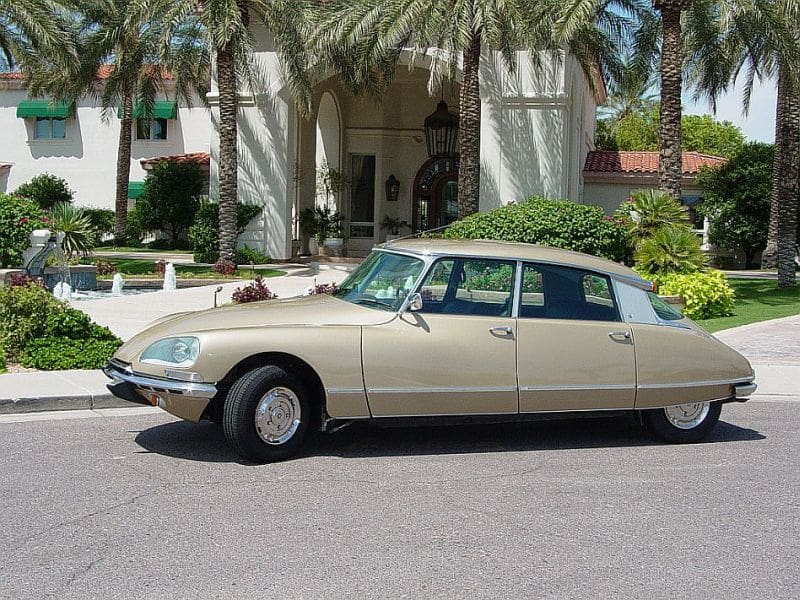 Classic beige Citroën DS parked in front of a palm tree-lined building.