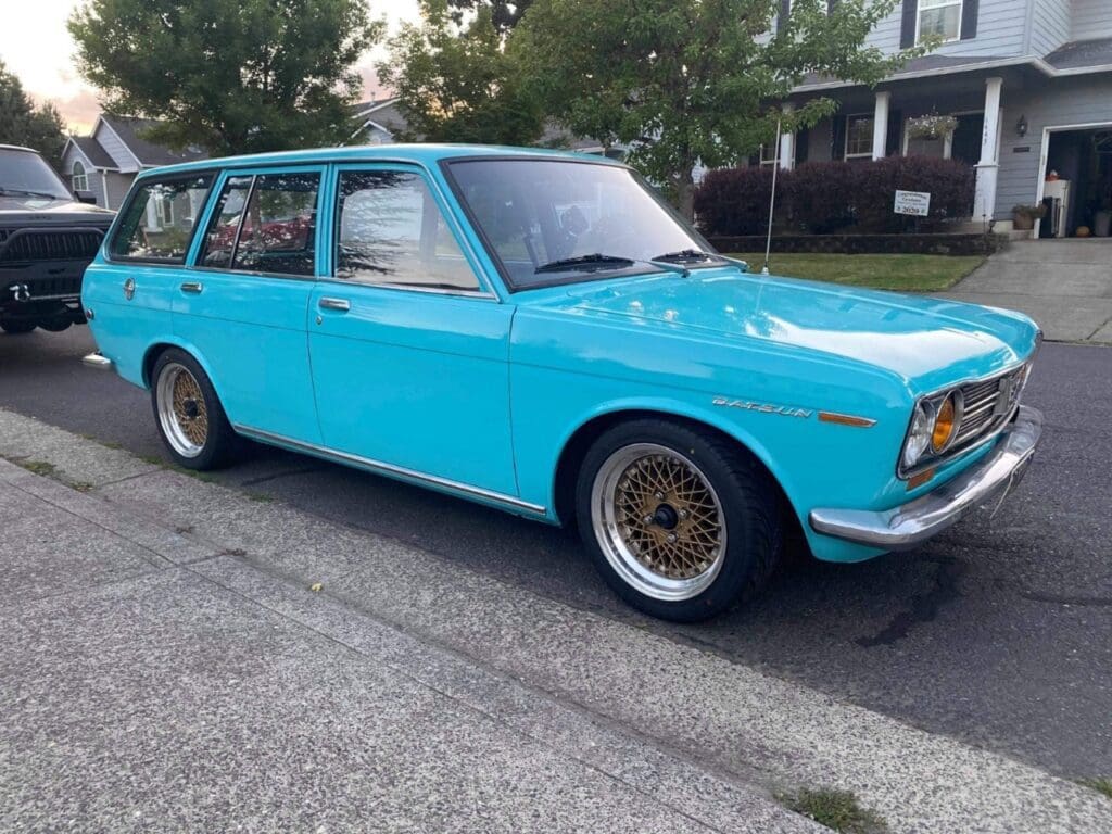 Classic turquoise station wagon with custom wheels parked on a driveway.