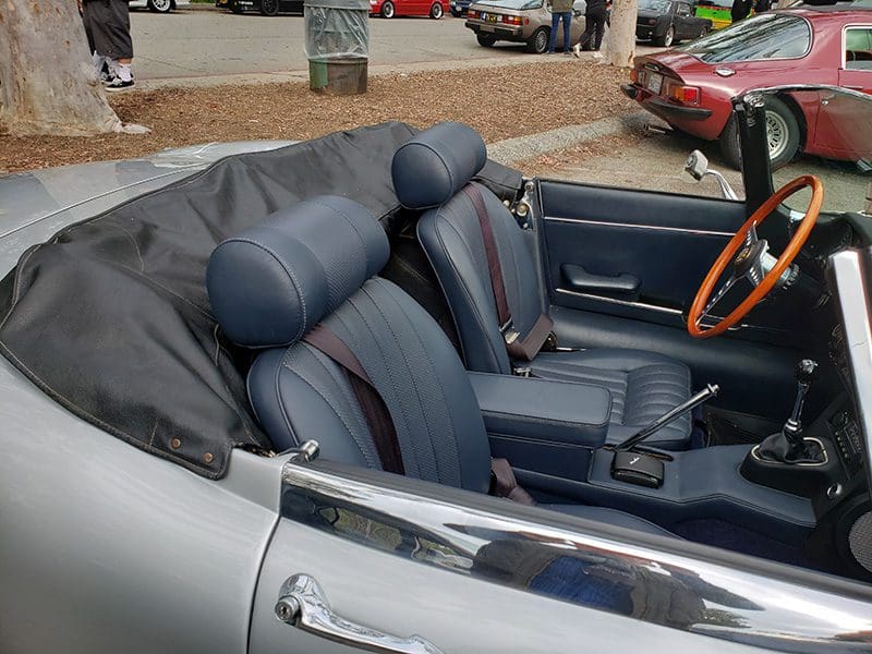 Luxury convertible car interior with leather seats and wooden steering wheel.