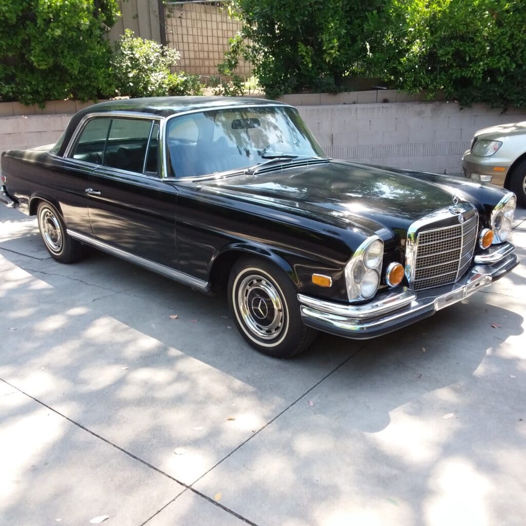 Classic black Mercedes-Benz coupe parked in a sunny driveway.