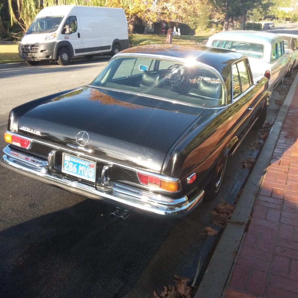 Classic black vintage car parked on a sunny street next to a sidewalk.