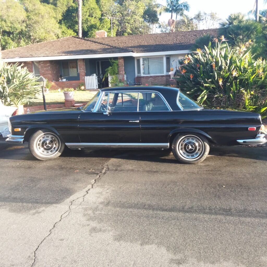 Classic black vintage car parked on a driveway in front of a house.