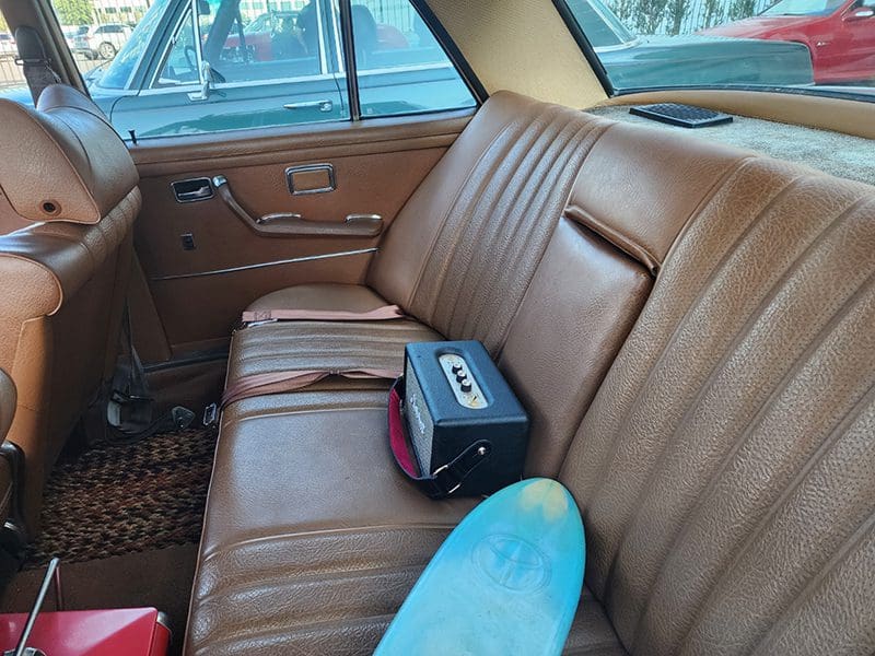 Brown leather car backseat with a blue skateboard and black bag.