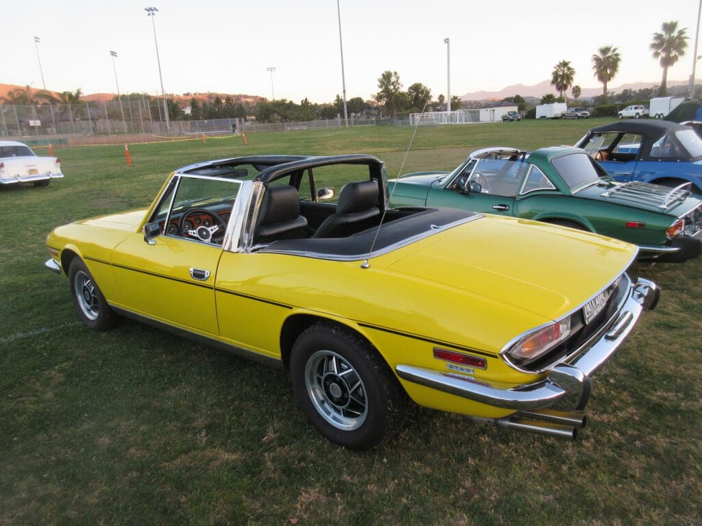 Classic yellow convertible car parked on grass near other vintage cars.