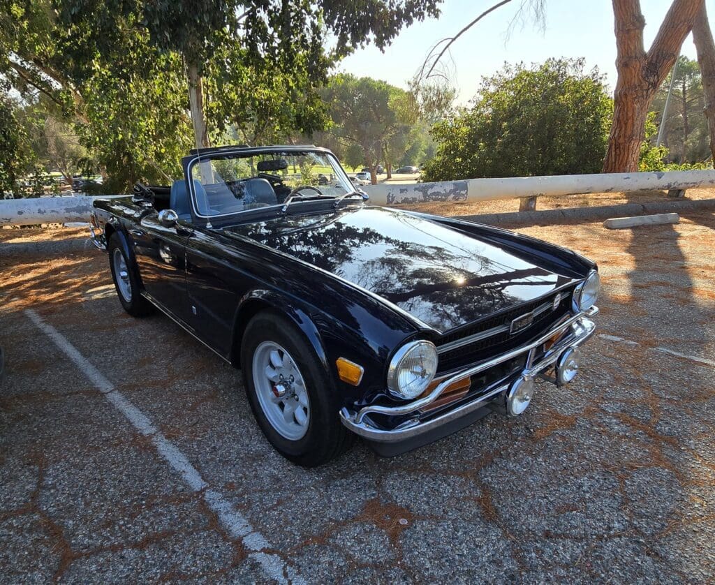 Classic black convertible sports car parked outdoors in sunlight.